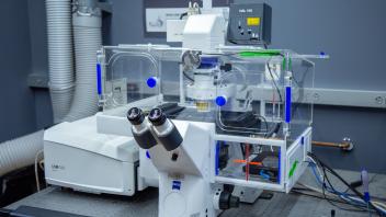 Confocal microscope with binocular eyepieces and transparent environmental chamber on a vibration-isolated table.